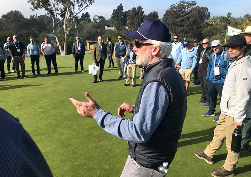A man wearing a ball cap and blue sweater holds a trophy