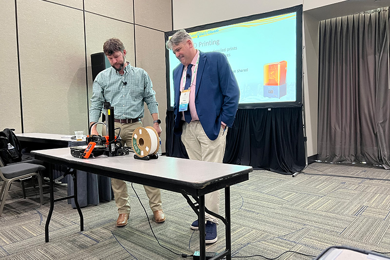 Two men in a conference room standing behind a 3d printer on a table