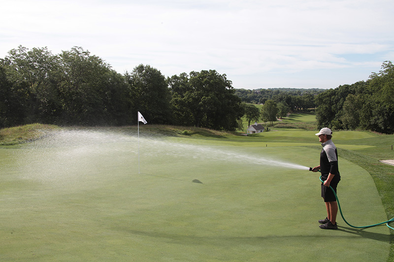 Man watering a golf course with a hose