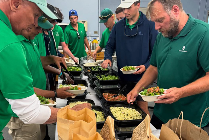 Group of golf course employees wearing green polos eating Chipotle in a maintenance office