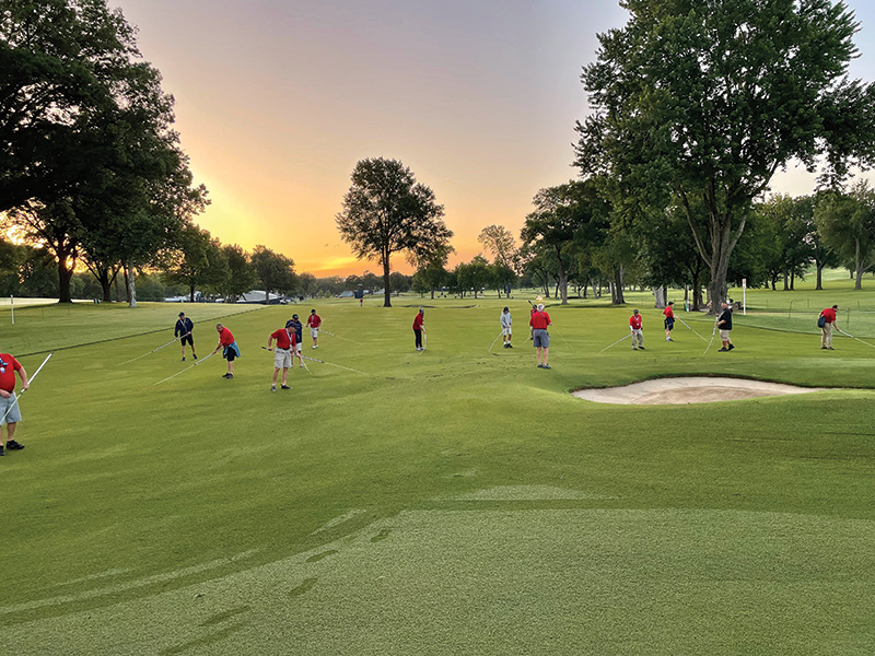 Tournament volunteers in red uniforms work on a golf course in the early morning