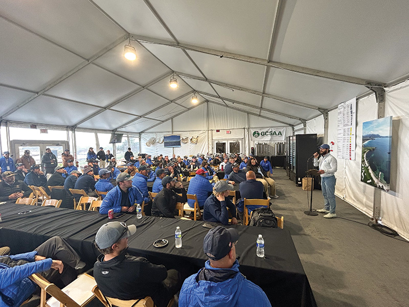 Volunteers gathering for a maintenance meeting in a tent, wearing blue uniform polos