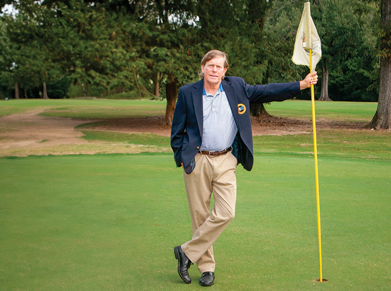 Greg Brooking standing next to a hole at Natchez Golf Club, holding a flag.