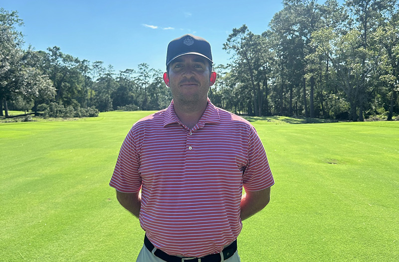 Mark Schulze on the course at Lochinvar Golf Club wearing a pink and white striped polo and dark baseball cap