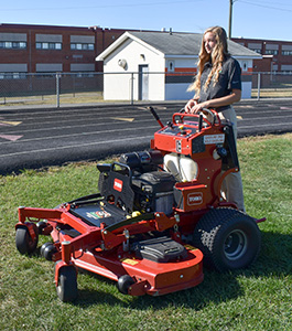 Julie Kessler, sitting on a riding mower on a football field.