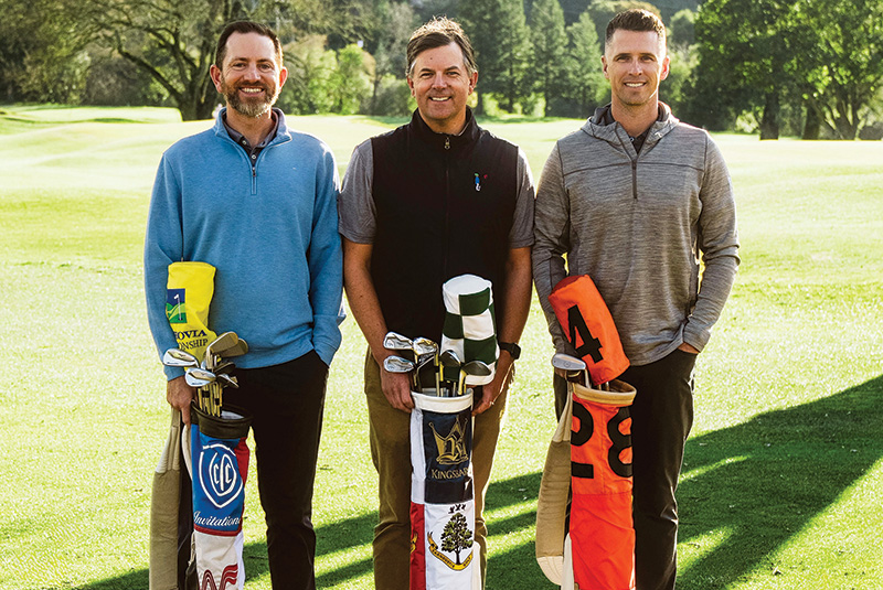 Three men carrying colorful golf bags standing on a golf course