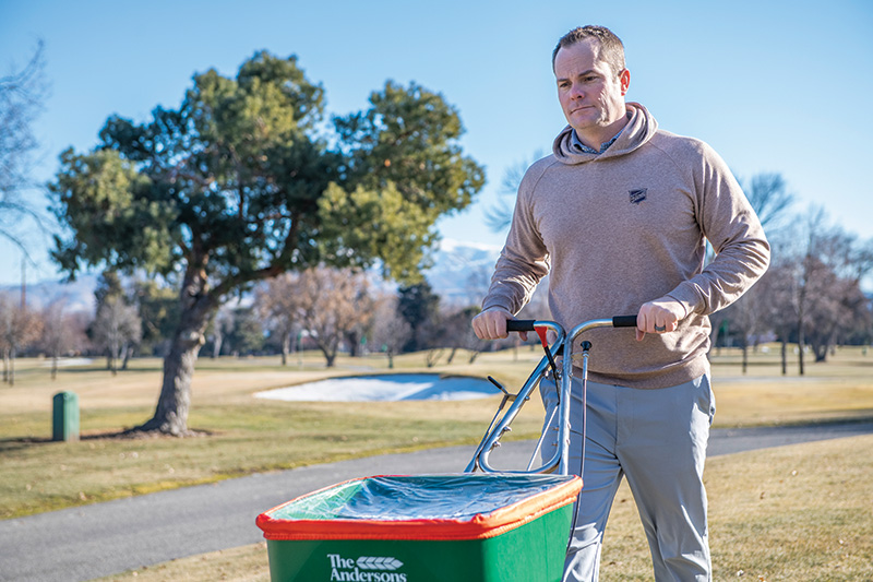 Man working outdoors pushing a green spreader