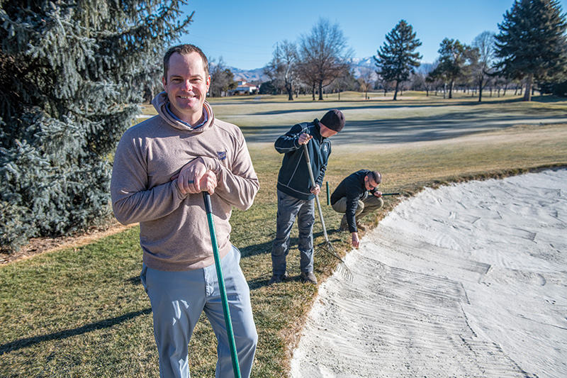 A man outdoors, smiling at the camera, with a golf course bunker in the background
