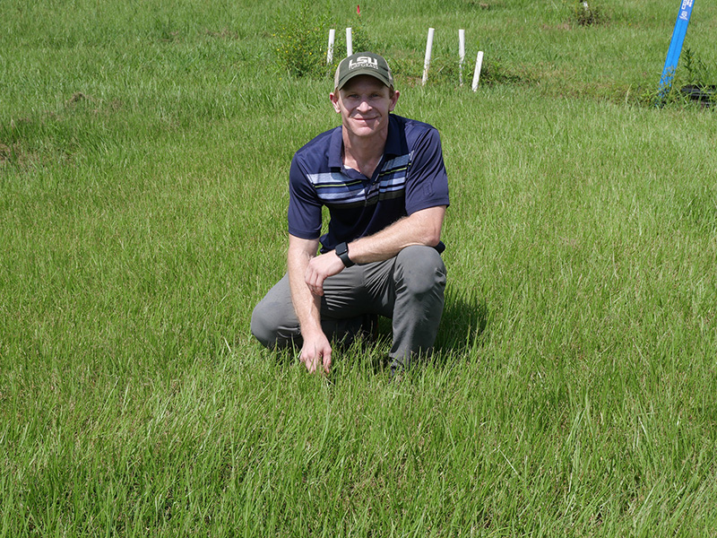 Eric DeBoer wearing a white ballcap and purple shirt in a turfgrass field