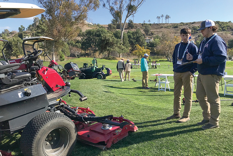 High school students on a golf course looking at a mower